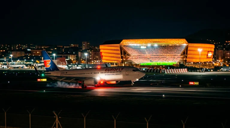 Avión comercial aterrizando de noche con un estadio de fútbol iluminado visible en el fondo