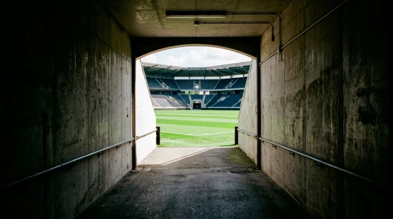 Túnel de vestuarios de un estadio de fútbol inglés vacío con luz natural entrando desde el campo verde al fondo